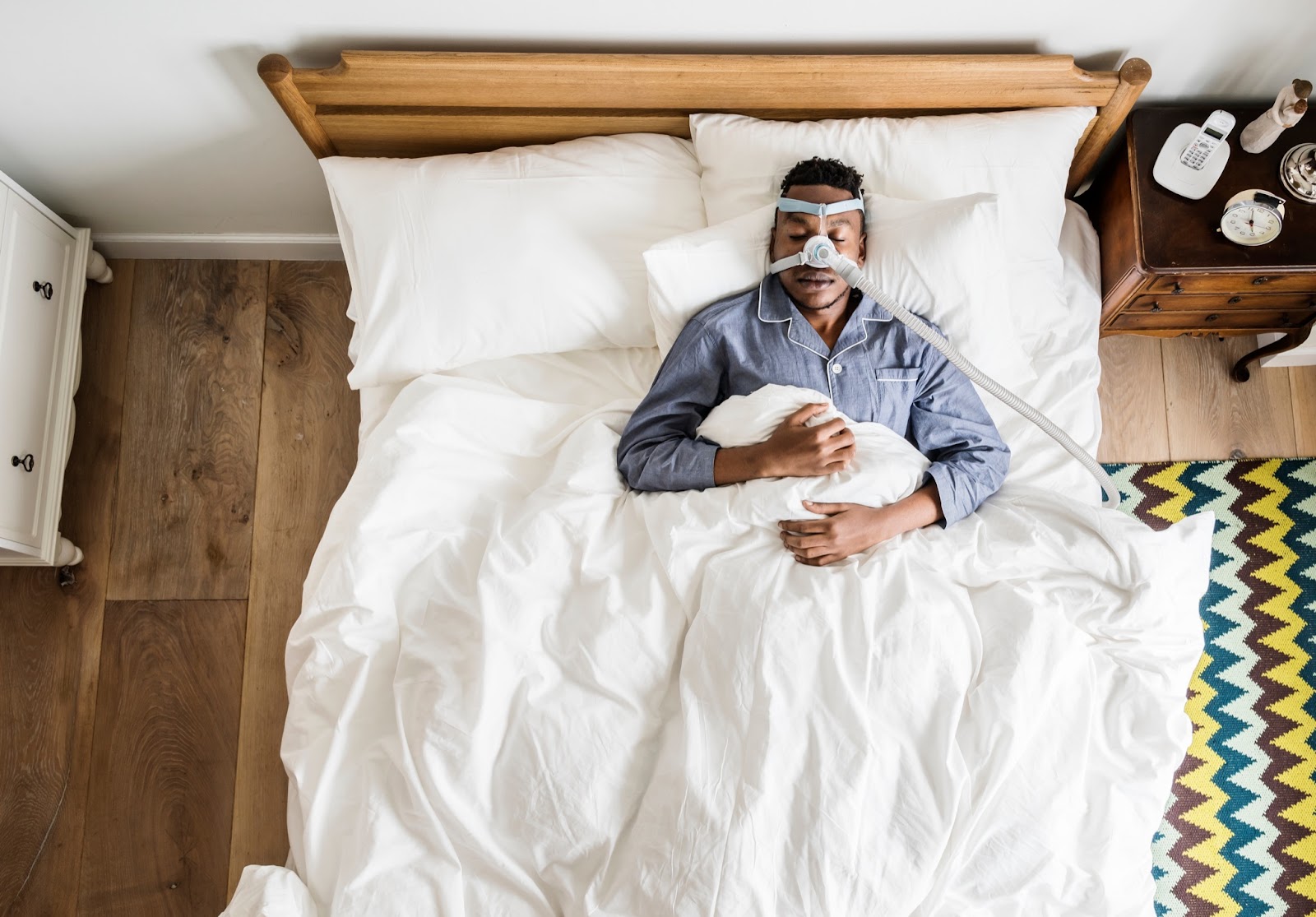 Aerial view of a man sleeping in his bed with a sleep apnea mask on his face.