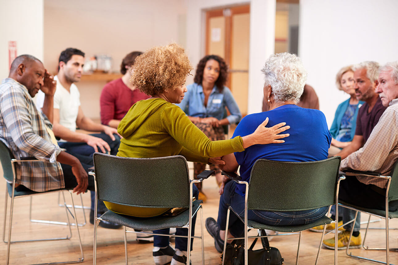 A group of people sit in a circle talking to one another in a support group.